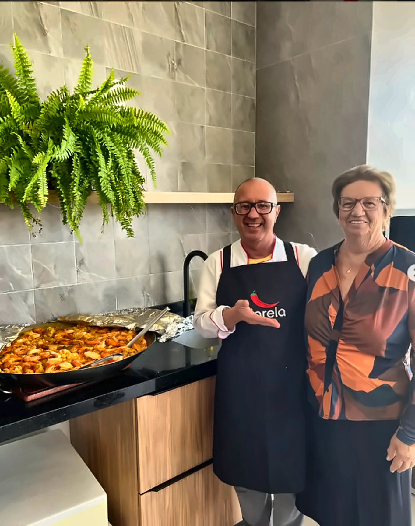 Chef Darela ao lado de cliente com paella de frutos do mar